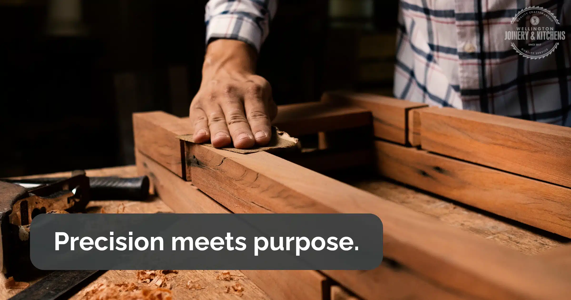 Man’s hand sanding timber surface in a wood workshop.